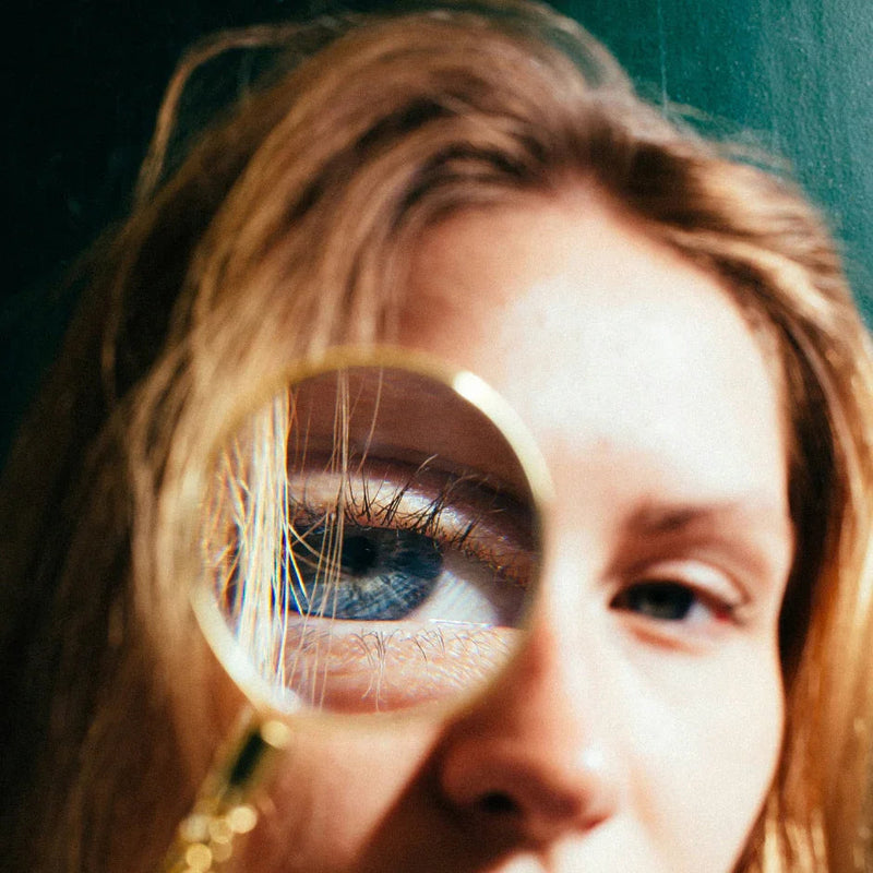 Close-up of a woman with blonde hair holding a magnifying glass highlighting her blue eye