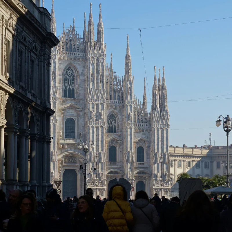 Crowd in front of Milan Cathedral with its detailed Gothic spires under clear blue sky