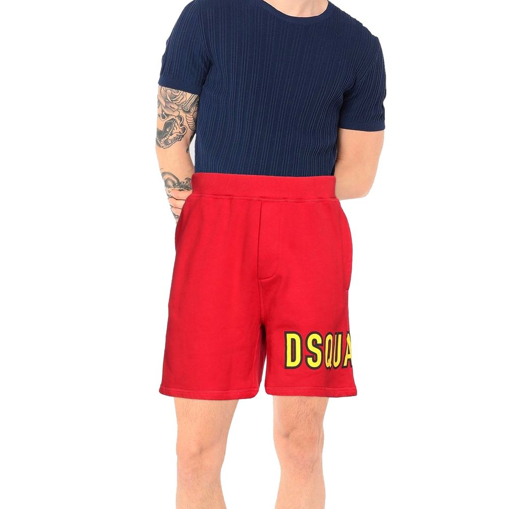 Man wearing red DSQUARED2 shorts and navy ribbed short-sleeve shirt, showcasing tattooed arms