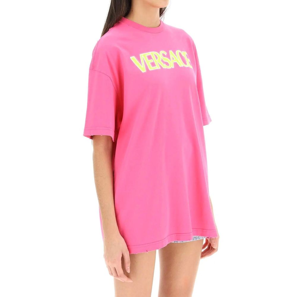 Woman wearing oversized bright pink Versace T-shirt with yellow logo on white background
